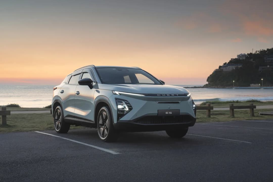 Chery E5 electric SUV in pale green front three-quarter at a beach car park at dusk