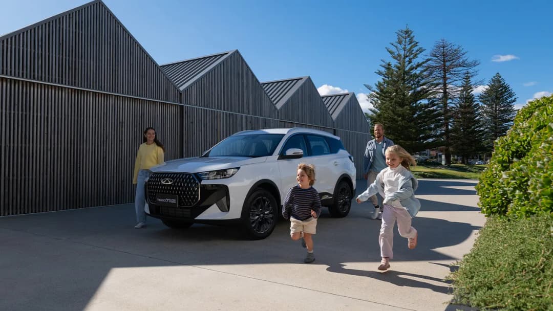Chery Tiggo 7 Super Hybrid in white front three-quarter with a family by timber sheds