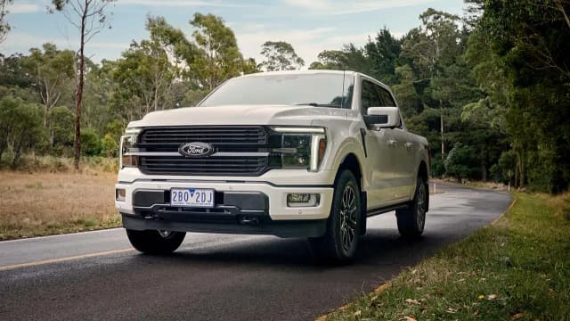 Ford F-150 Platinum in white driving on a tree lined country road