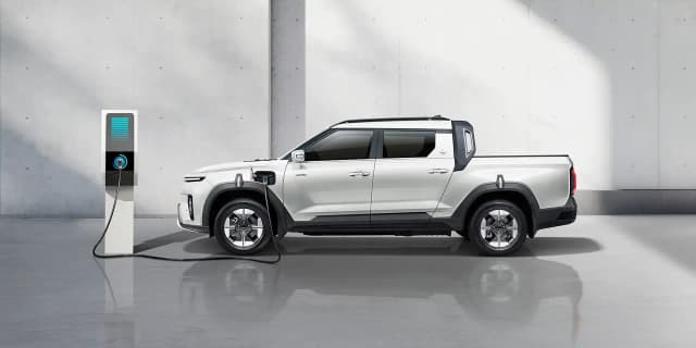 KGM Musso EV in white charging at a wall charger, side view