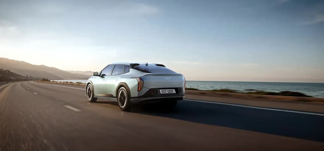 Kia EV4 electric hatch in silver driving on a coastal road, rear three-quarter view
