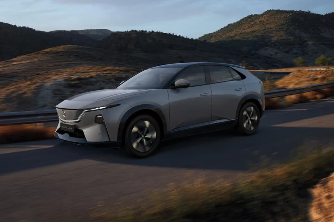 Mazda CX-6e electric SUV in grey driving on a hillside road, front three-quarter view