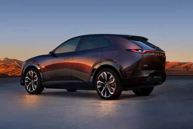 Mazda CX-6e in dark purple at dusk with mountains behind, rear three-quarter view