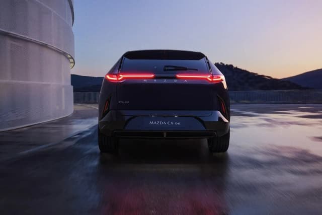 Mazda CX-6e from behind with full width light bar on a wet road at dusk