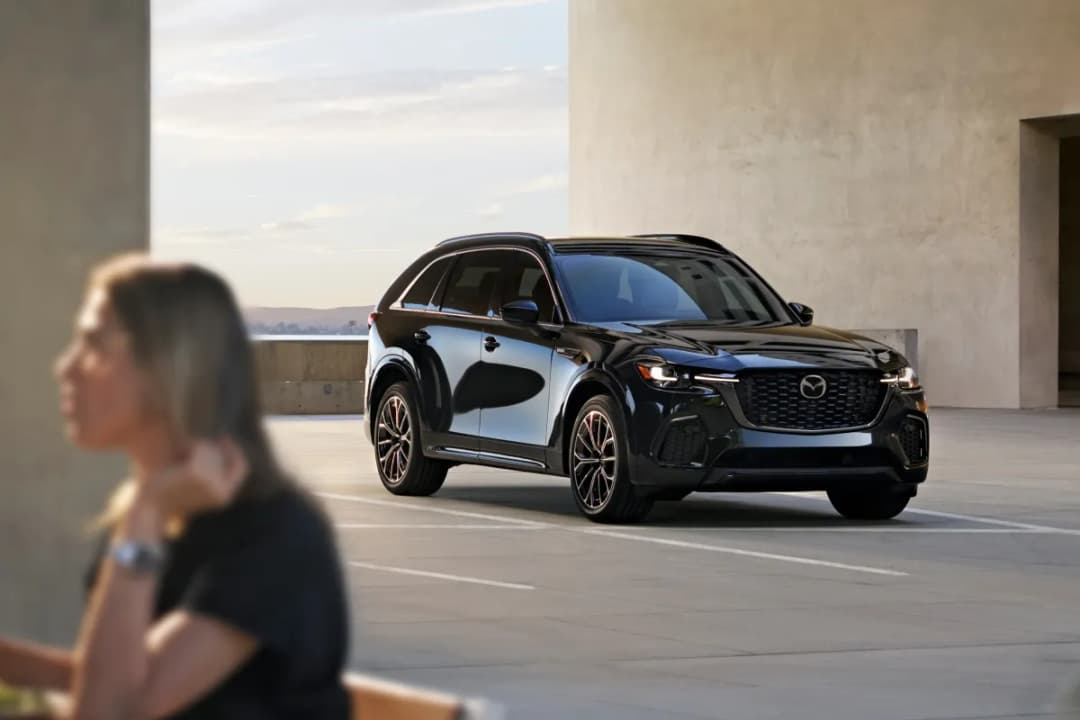 Mazda CX-70 in black parked by a concrete building, front three-quarter view