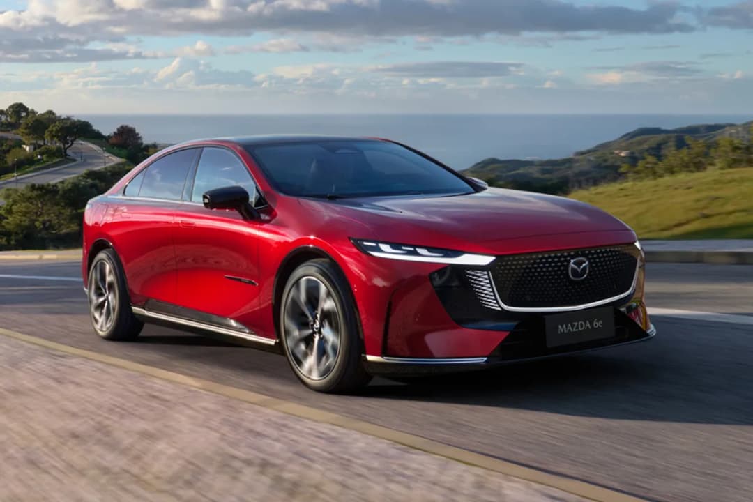 Mazda 6e electric liftback in Soul Red on a coastal road, front three-quarter view