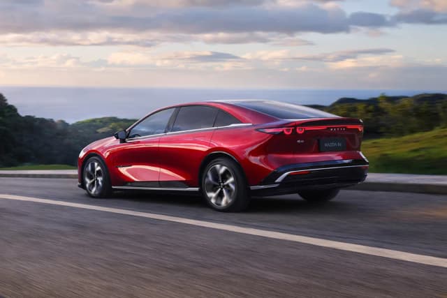 Mazda 6e in Soul Red on a coastal road, rear three-quarter view