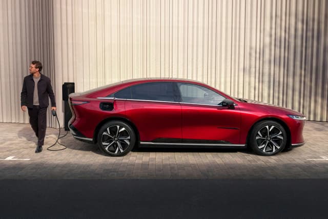Mazda 6e in Soul Red plugged into a wall charger, side view