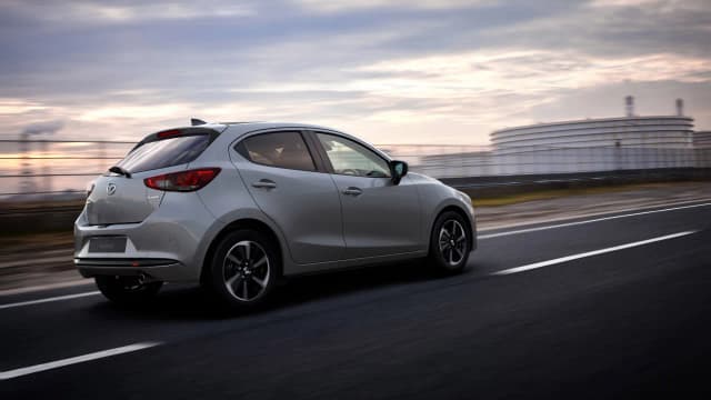 Mazda2 hatch in silver driving on a coastal road, rear three-quarter view