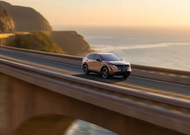 Nissan Ariya driving on a coastal bridge at sunset