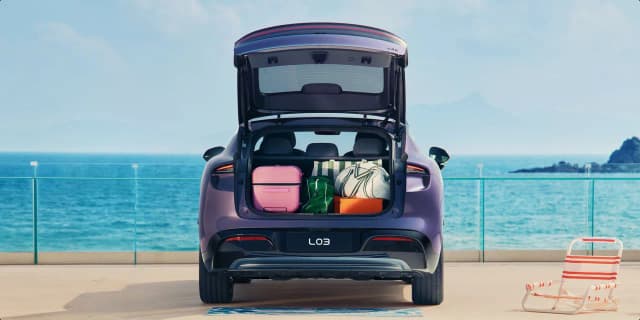 XPeng L03 rear view with the power tailgate open and luggage in the boot by the sea